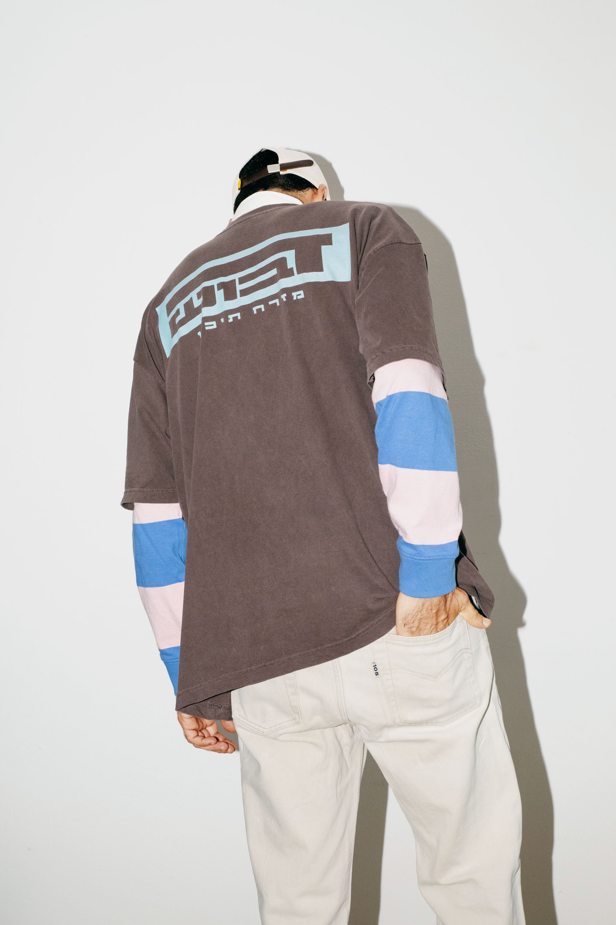 A model wearing an oversized DABUSH t-shirt in washed brown, made from 100% cotton.
דוגמן לובש טישרט אוברסייז של דבוש בצבע חום שטוף, עשויה 100% כותנה עם לוגו בצבע תכלת.