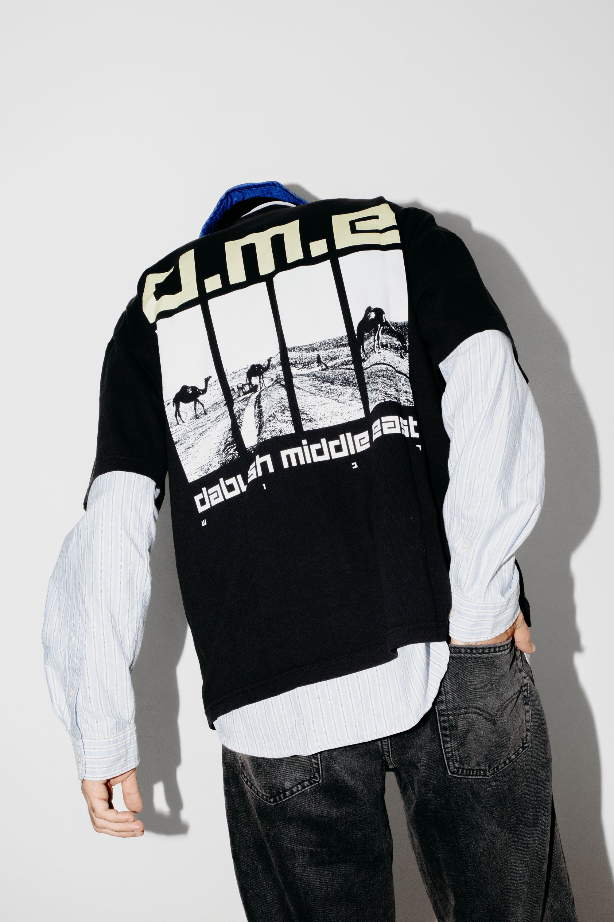 A model's back wearing an oversized DABUSH t-shirt in black, made from 100% cotton, with printed graphics Dabush Middle East.
דוגמן לובש אוברסייז טישרט של דבוש בצבע שחור, עשויה 100% כותנה עם  גרפיקה ענקית מקדימה ומאחורה.
