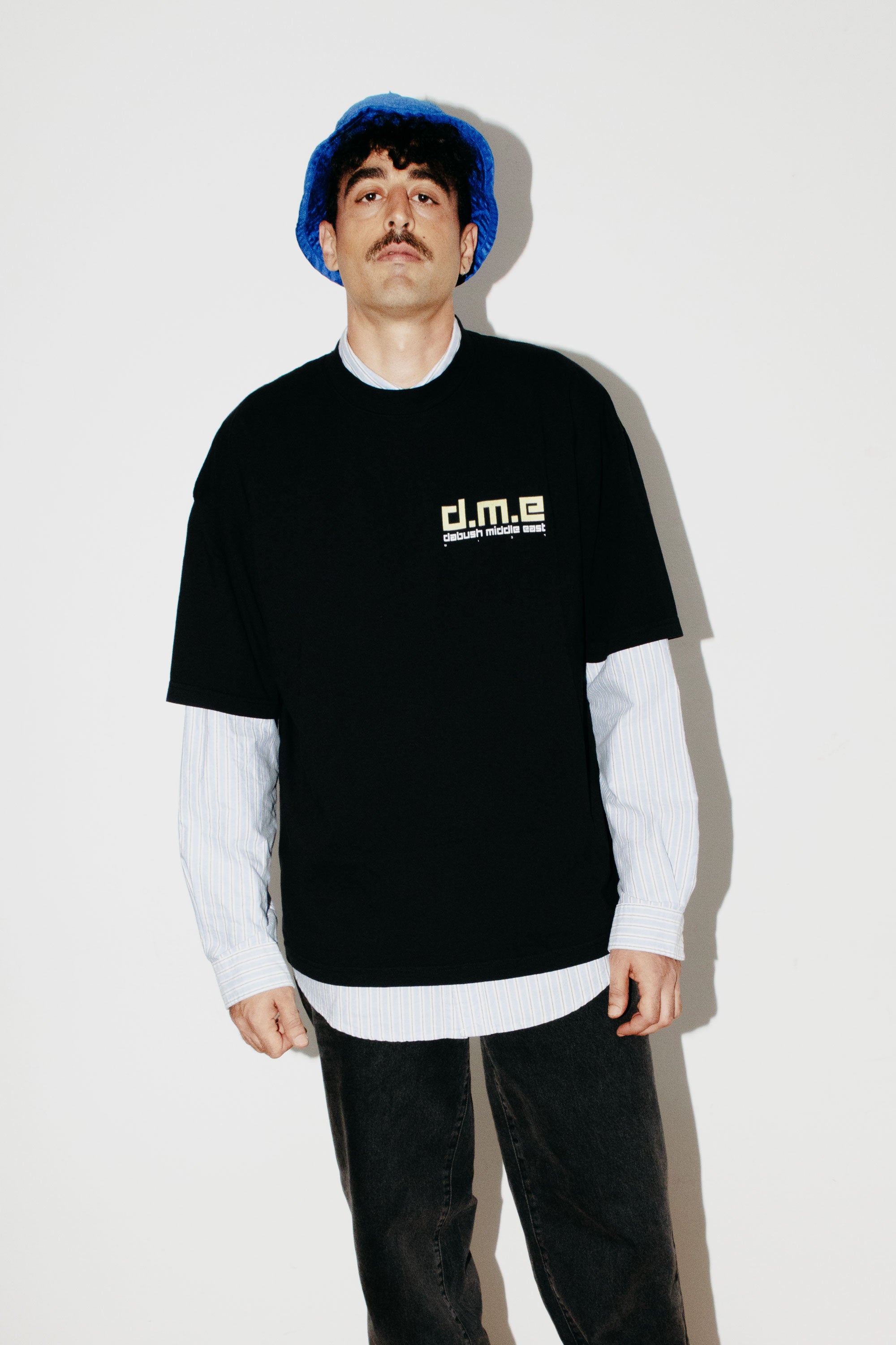 A model wearing an oversized DABUSH t-shirt in black, made from 100% cotton, with printed graphics Dabush Middle East.
דוגמן לובש אוברסייז טישרט של דבוש בצבע שחור, עשויה 100% כותנה עם גרפיקה ענקית מקדימה ומאחורה.