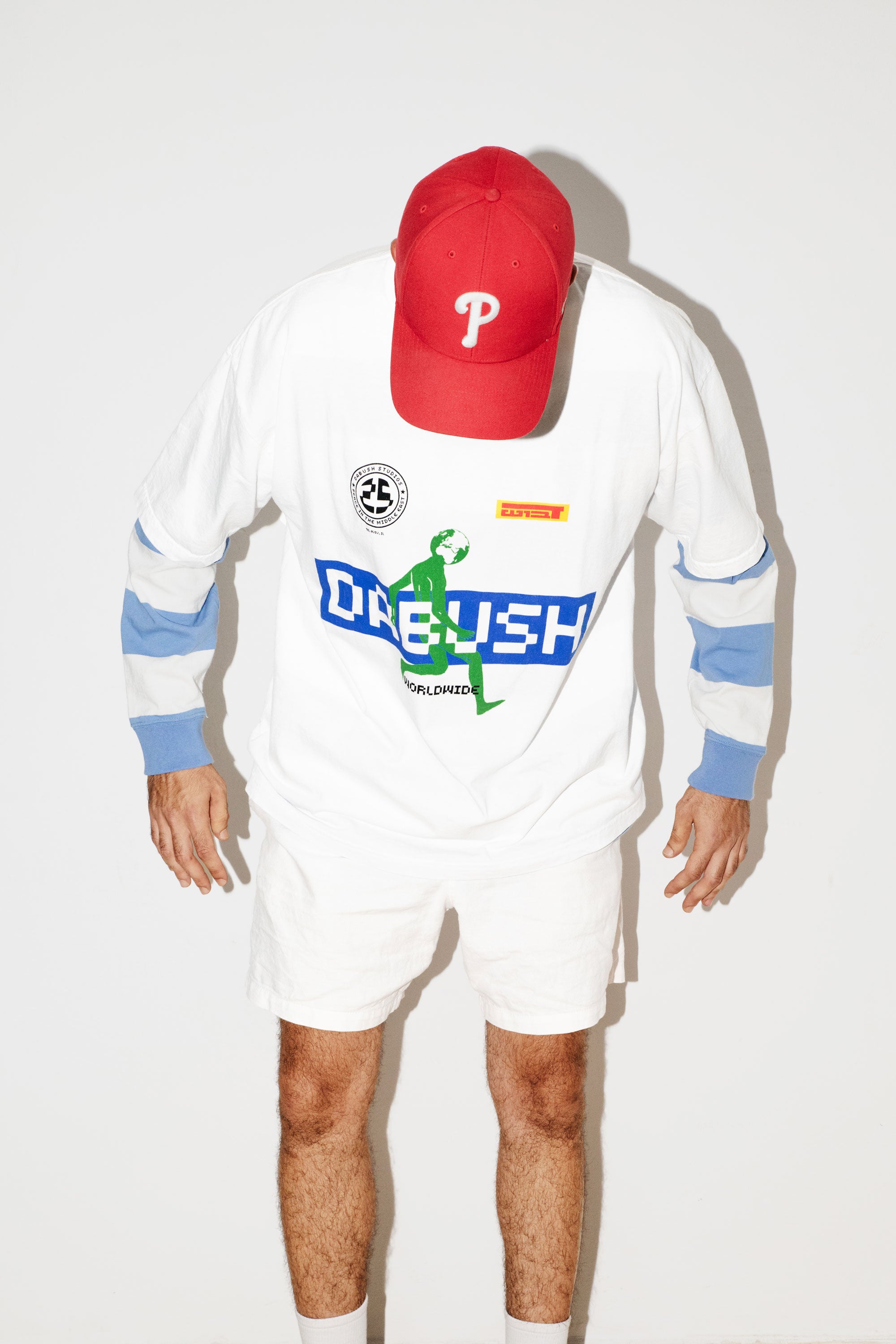 A model wearing an oversized DABUSH t-shirt in white, made from 100% cotton.
דוגמן לובש טישרט אוברסייז של דבוש בצבע לבן, עשויה 100% כותנה עם גרפיקה צבעונית.