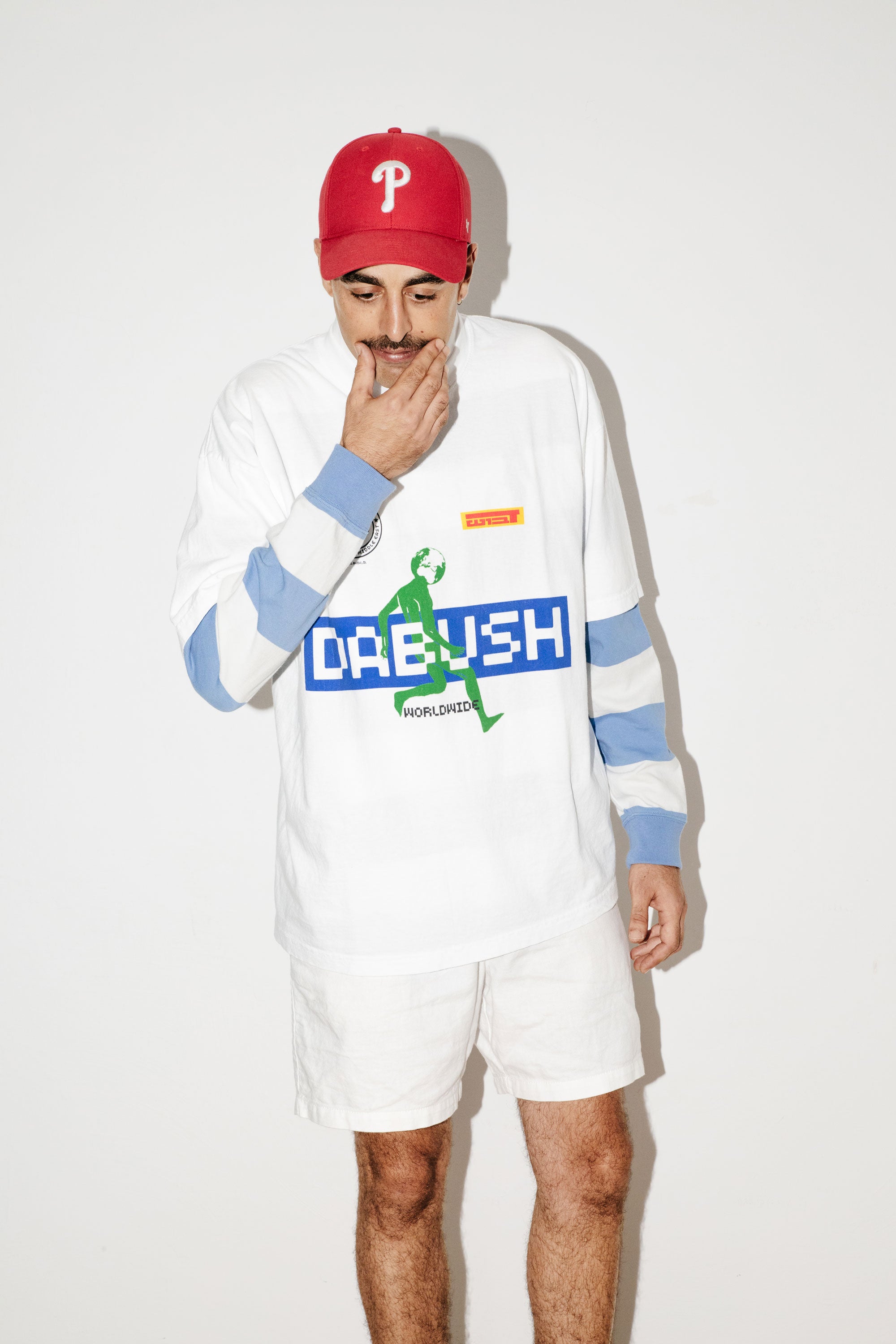 A model wearing an oversized DABUSH t-shirt in white, with colorful graphics, made from 100% cotton.

דוגמן לובש טישרט אוברסייז של דבוש בצבע לבן, עשויה 100% כותנה עם גרפיקה צבעונית.

